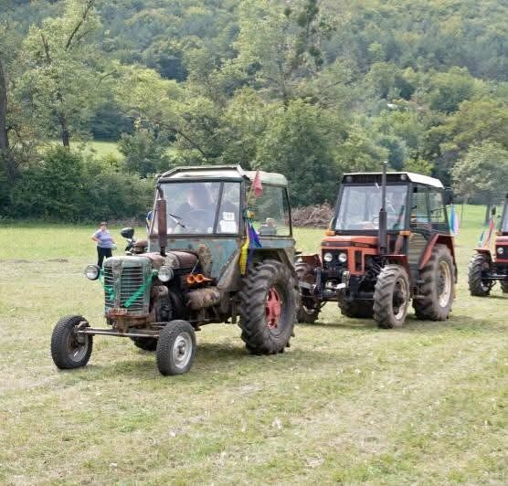 Prehliadka historických traktorov na lúke, v popredí zelený traktor so zástavkou, v pozadí zalesnený svah